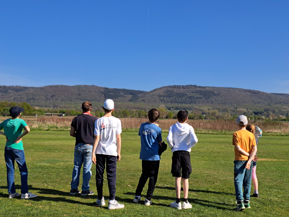 Jugendliche stehen auf dem Flugplatz und beobachten Modellflugzeuge.